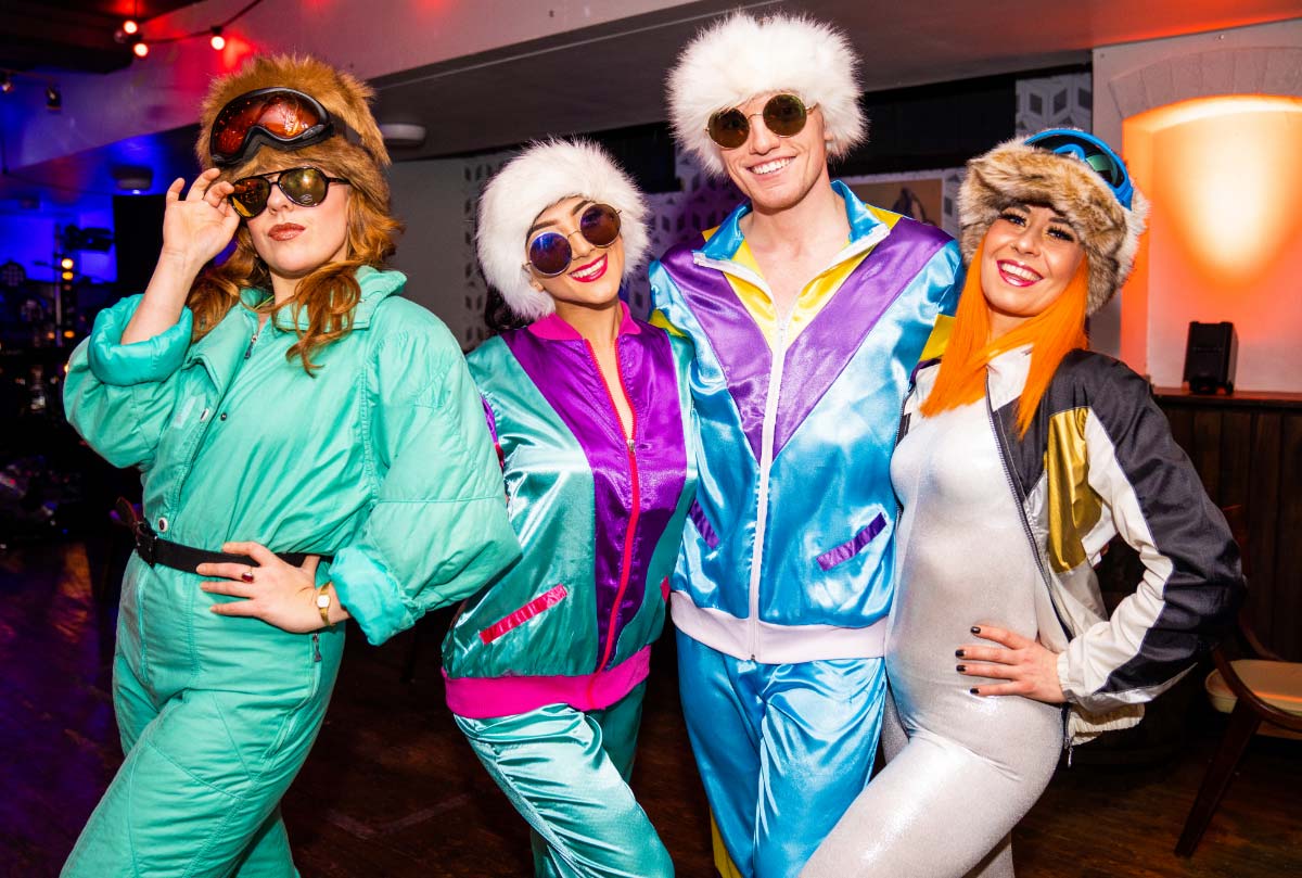 Four friends in vibrant retro ski outfits with goggles posing confidently at an AV Production and Entertainment themed party.