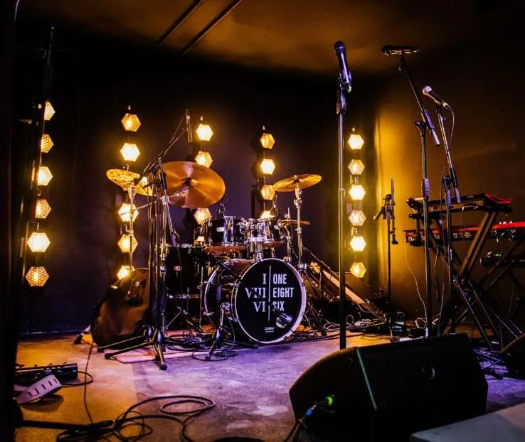 An empty stage set for a performance with a drum kit at the center, surrounded by atmospheric lighting from AV Installations Manchester, waiting for the musicians to bring it to life.