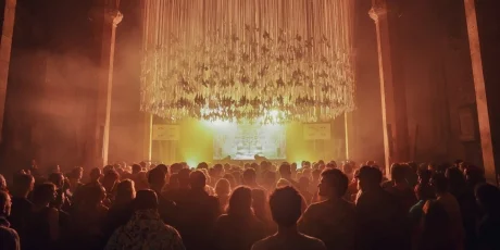 A crowd of people gathered under a grand chandelier, basking in the warm, ambient light provided by AV Events Hire at an indoor event.