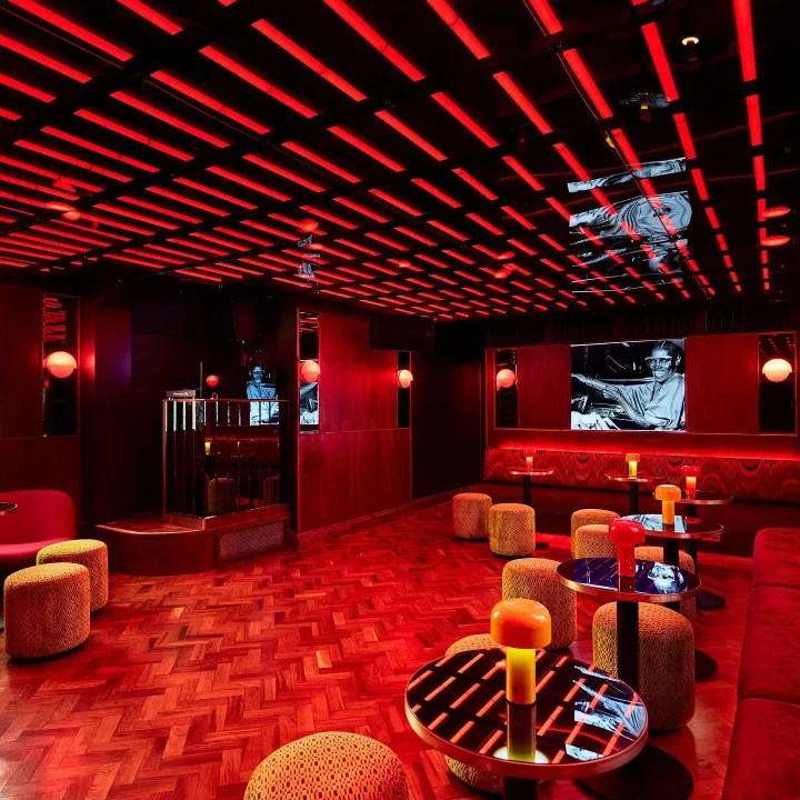 A sleek and modern lounge with vibrant red lighting installations, geometric ceiling design, and stylish furniture, exuding a sophisticated and intimate atmosphere.