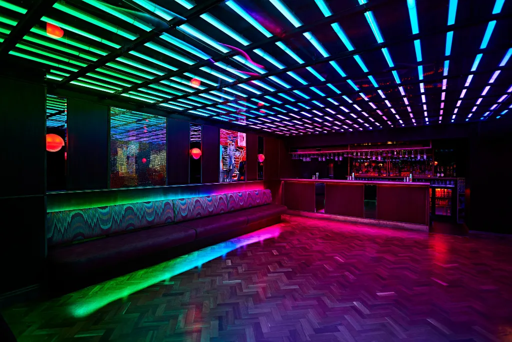 Modern nightclub interior with vibrant neon lights and geometric patterns creating a futuristic atmosphere, enhanced by a state-of-the-art AV installation for venues.