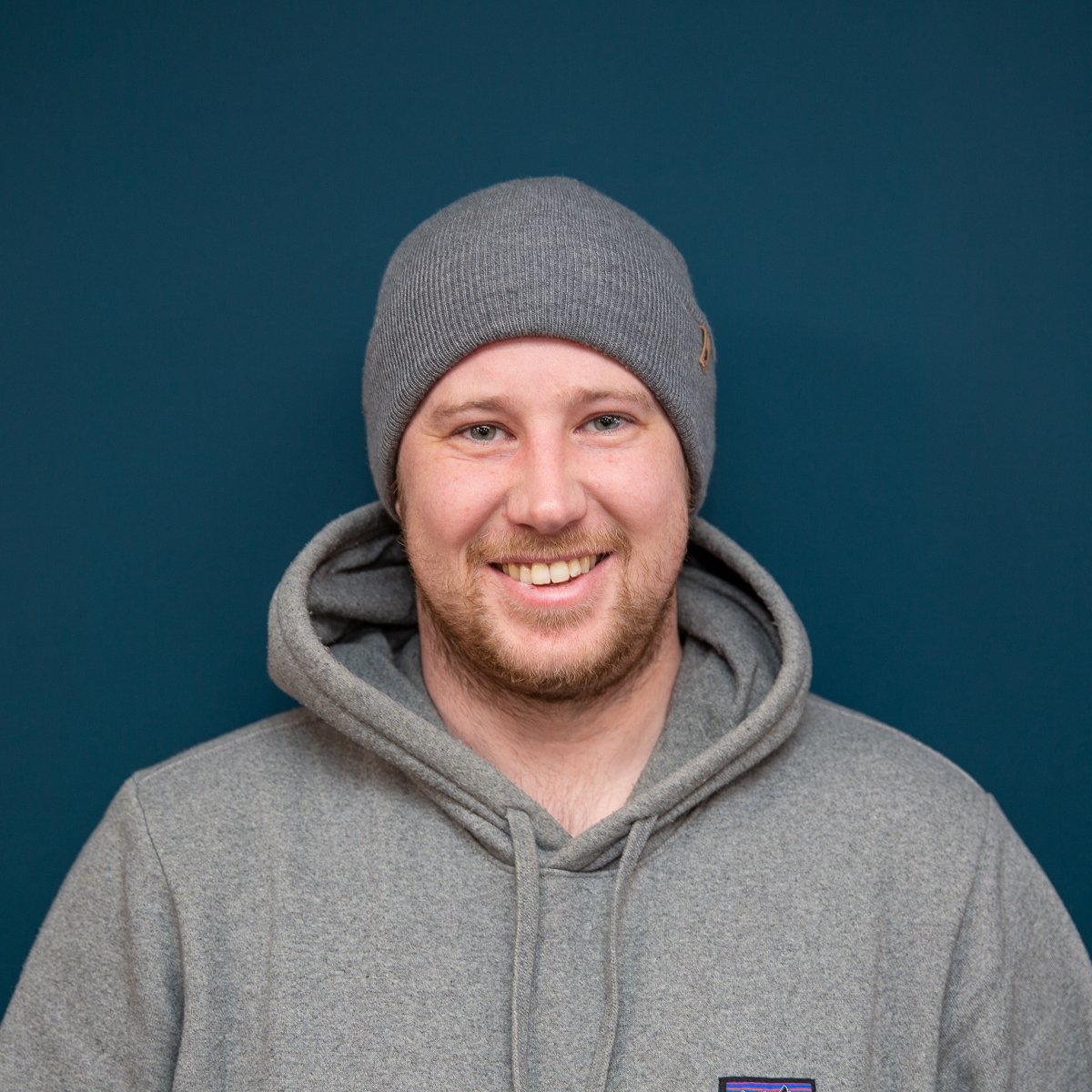 A smiling man in a gray hoodie and beanie against a blue background, representing an AV company.
