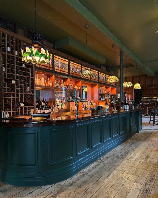 A warm and inviting traditional bar and restaurant with a classic wooden decor, illuminated by tiffany-style pendant lights, featuring a well-stocked liquor shelf, advanced AV installation for entertainment, and a cozy ambiance